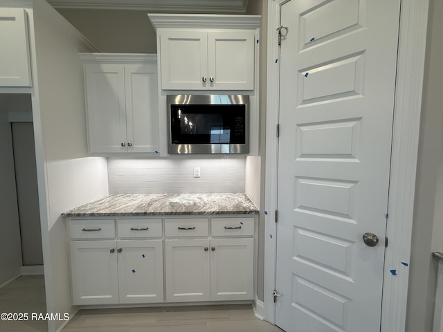 205 Keystone Dr, Scott, LA 70583 - kitchen featuring stainless steel microwave, white cabinetry, decorative backsplash, and light stone countertops
