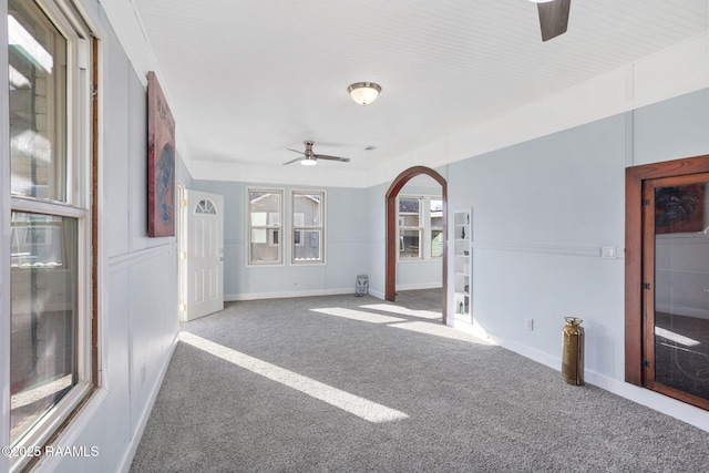 carpeted empty room with arched walkways, ceiling fan, and baseboards