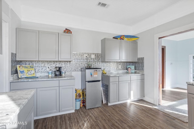 kitchen with decorative backsplash, visible vents, dark wood finished floors, gray cabinetry, and freestanding refrigerator
