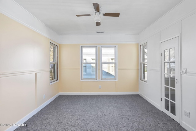 empty room featuring crown molding, baseboards, carpet floors, visible vents, and a ceiling fan