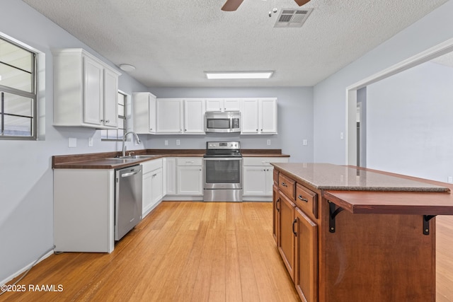kitchen featuring dark countertops, visible vents, stainless steel appliances, light wood finished floors, and a sink