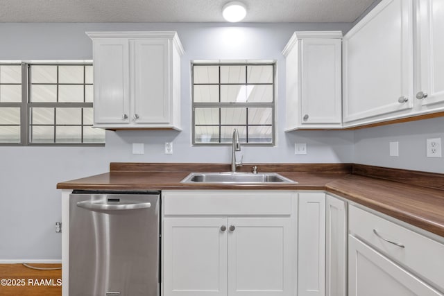 kitchen featuring stainless steel dishwasher, white cabinetry, a sink, and a textured ceiling