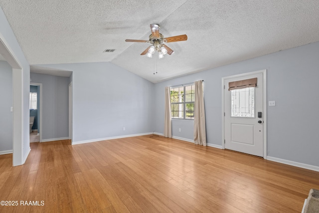 unfurnished living room with baseboards, vaulted ceiling, light wood-type flooring, a textured ceiling, and ceiling fan