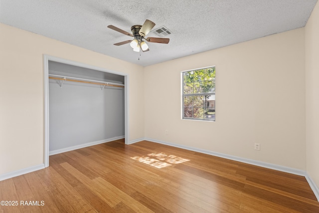 unfurnished bedroom with baseboards, a closet, a textured ceiling, visible vents, and light wood finished floors