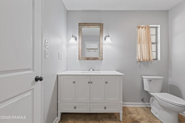 bathroom with toilet, a textured ceiling, vanity, and baseboards