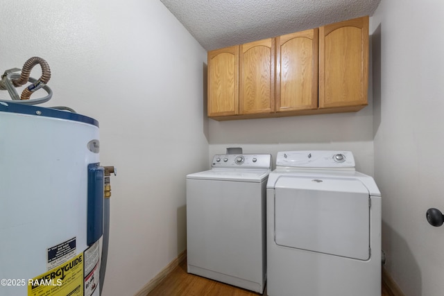 clothes washing area featuring a textured ceiling, electric water heater, wood finished floors, cabinet space, and washer and clothes dryer