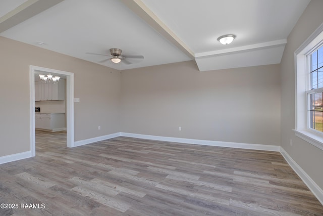 empty room featuring ceiling fan with notable chandelier, baseboards, and wood finished floors