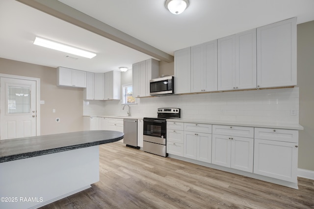 kitchen featuring beam ceiling, light wood finished floors, appliances with stainless steel finishes, and backsplash