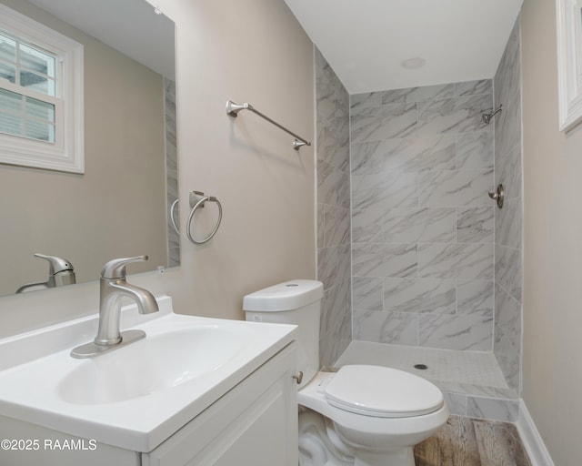 full bath featuring toilet, wood finished floors, tiled shower, and vanity