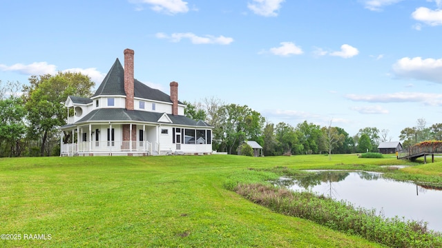 back of house featuring a sunroom, covered porch, a lawn, a water view, and a chimney