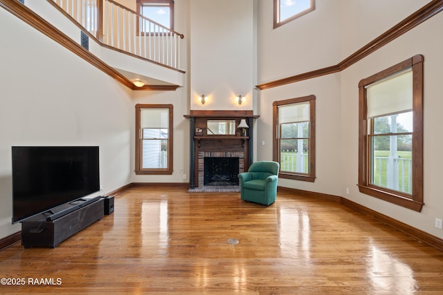 unfurnished living room featuring a high ceiling, wood finished floors, baseboards, and a brick fireplace