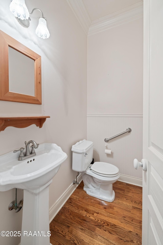 half bathroom with ornamental molding, a wainscoted wall, toilet, wood finished floors, and baseboards