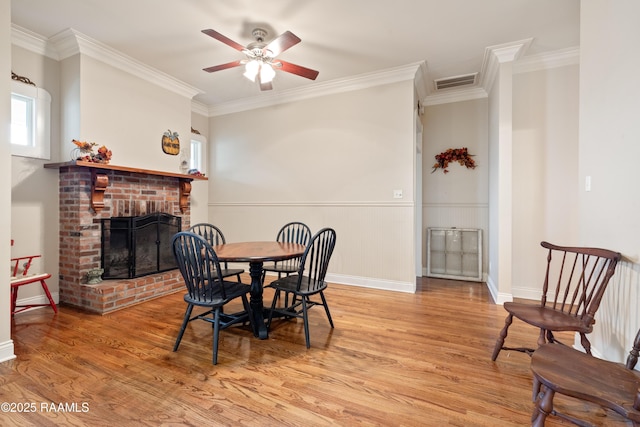 dining area featuring light wood-style floors, ornamental molding, a ceiling fan, visible vents, and a brick fireplace
