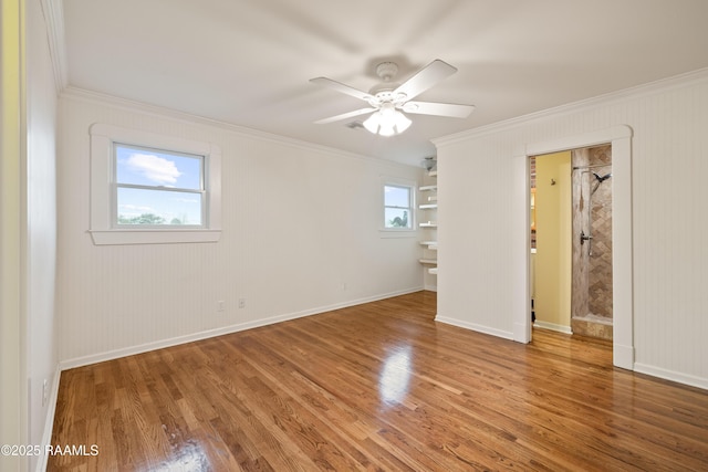 empty room with a ceiling fan, wood finished floors, baseboards, and ornamental molding