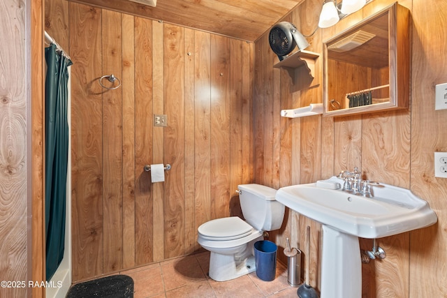 bathroom with toilet, tile patterned floors, wood walls, and curtained shower
