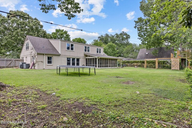 back of house with a fenced backyard, a yard, central AC, a sunroom, and a trampoline