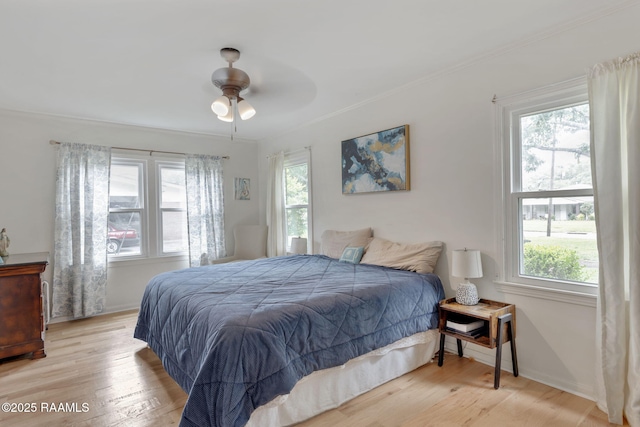 bedroom featuring wood finished floors, crown molding, a ceiling fan, and multiple windows