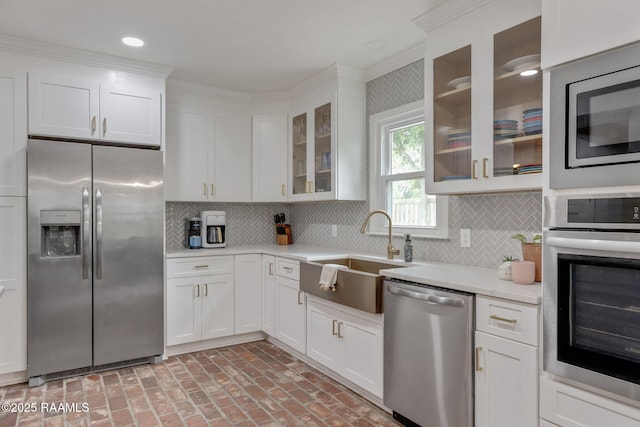 kitchen with stainless steel appliances, light countertops, a sink, brick floor, and white cabinetry