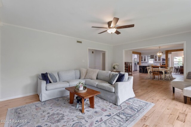 living room with crown molding, light wood-style flooring, visible vents, and ceiling fan with notable chandelier