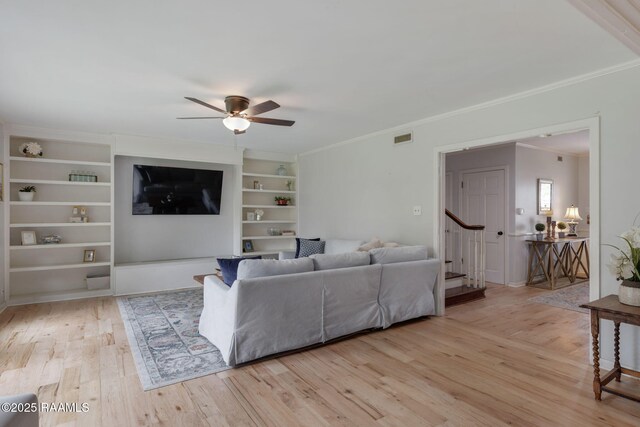 living area with wood finished floors, visible vents, a ceiling fan, ornamental molding, and stairs