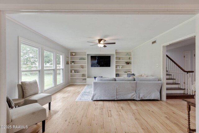 living room with a ceiling fan, crown molding, built in features, light wood-style flooring, and visible vents