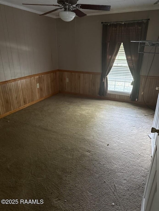 empty room with wooden walls, carpet floors, ceiling fan, and a wainscoted wall