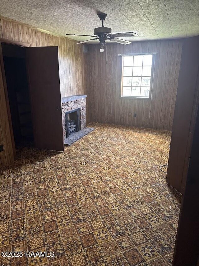 unfurnished living room featuring a fireplace with raised hearth, wood walls, and a ceiling fan