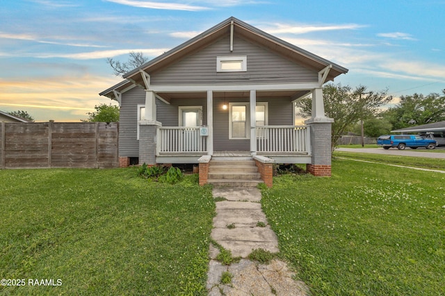 view of front facade featuring covered porch, fence, and a yard