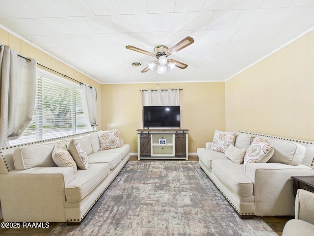 living room featuring a ceiling fan, crown molding, wood finished floors, wooden walls, and visible vents