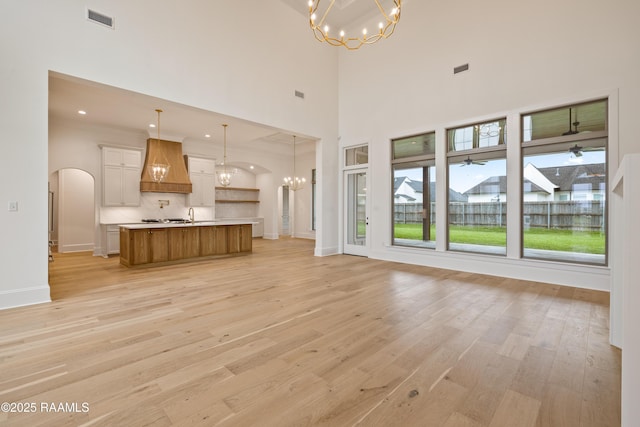 207 Sunset Palm Ct, Youngsville, LA 70592 - unfurnished living room featuring a chandelier, light wood-style flooring, arched walkways, and a towering ceiling