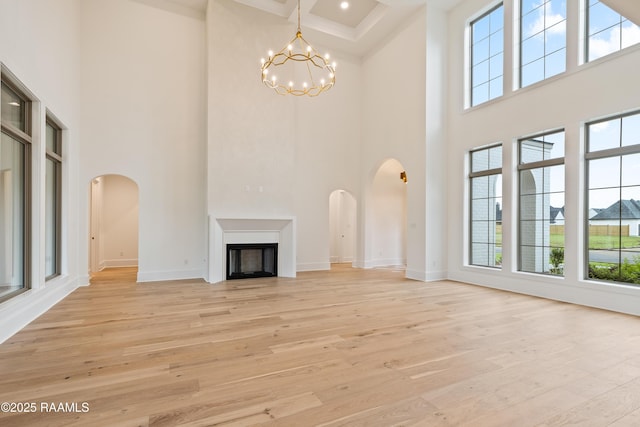 207 Sunset Palm Ct, Youngsville, LA 70592 - unfurnished living room featuring a towering ceiling, arched walkways, a chandelier, light wood finished floors, and a fireplace