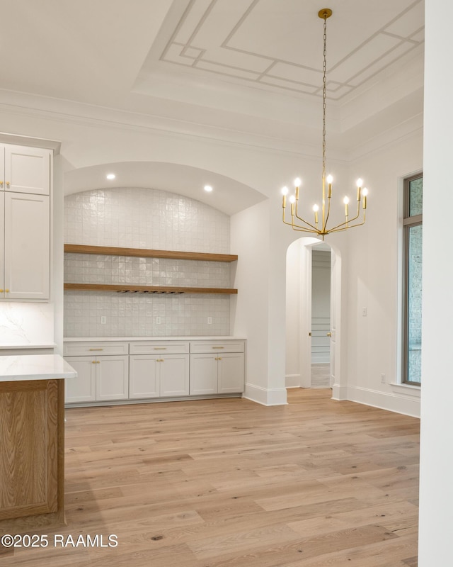 207 Sunset Palm Ct, Youngsville, LA 70592 - unfurnished dining area featuring arched walkways, a tray ceiling, light wood-type flooring, ornamental molding, and a chandelier