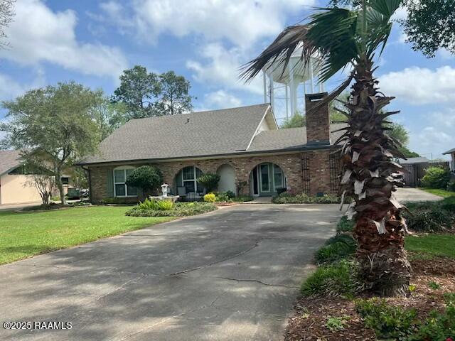 view of front facade with a chimney, concrete driveway, and a front lawn