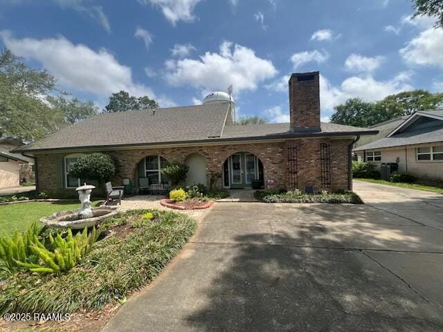 view of front of home featuring brick siding, driveway, a chimney, and cooling unit