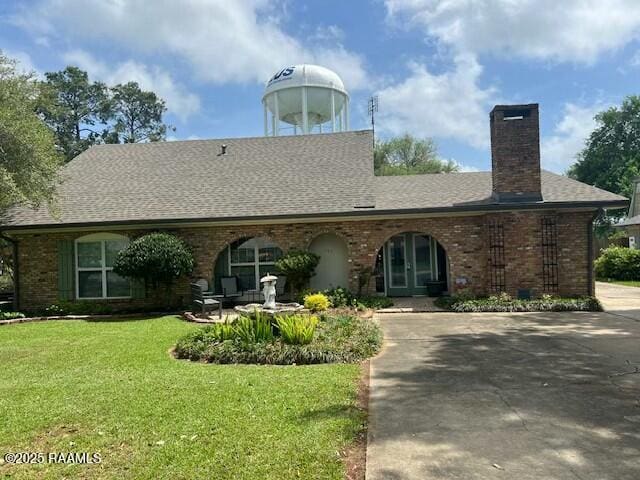 view of front of house featuring a shingled roof, a chimney, a front lawn, and brick siding