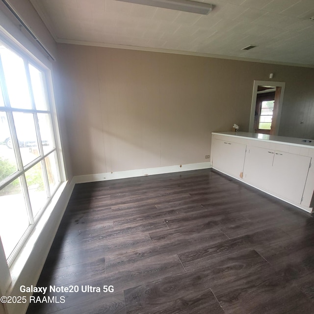 unfurnished room with dark wood finished floors, ornamental molding, and a wealth of natural light