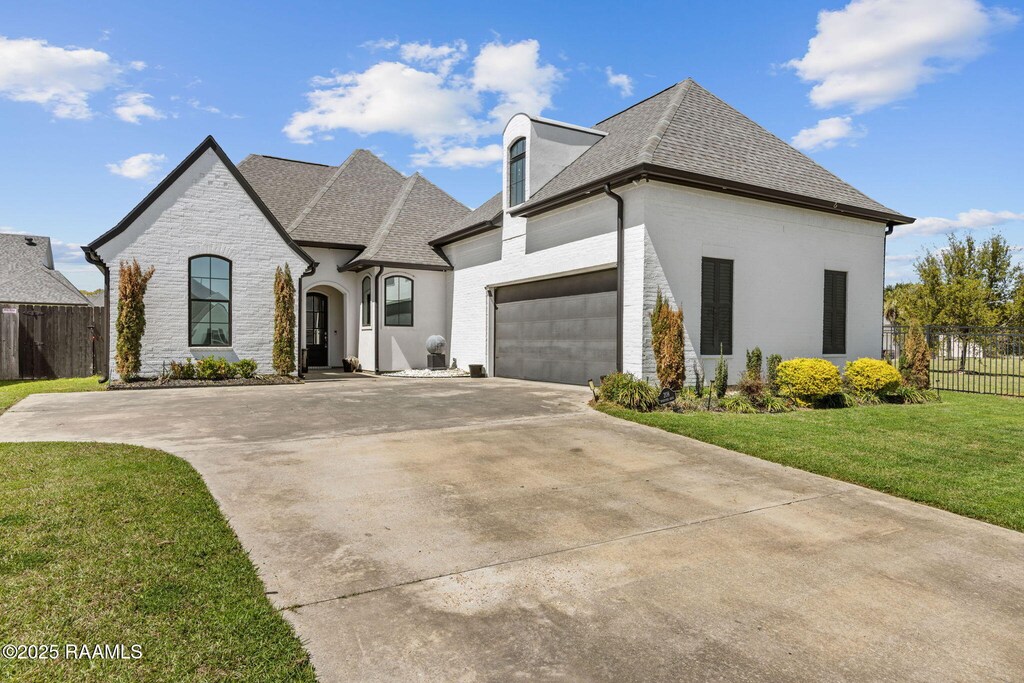 208 Woodstone Dr, Lafayette, LA 70508 - french provincial home featuring a shingled roof, a garage, fence, a front lawn, and driveway