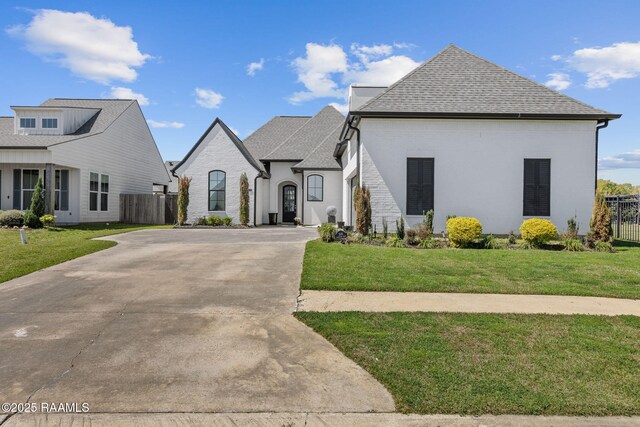 208 Woodstone Dr, Lafayette, LA 70508 - french country inspired facade featuring roof with shingles, concrete driveway, a front yard, and fence