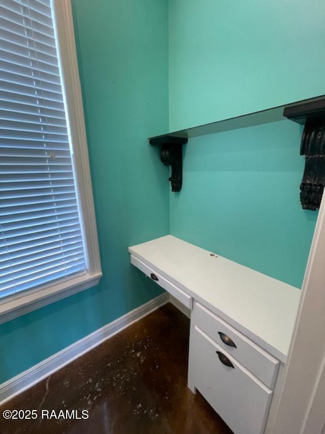 unfurnished office featuring concrete floors, built in study area, and baseboards