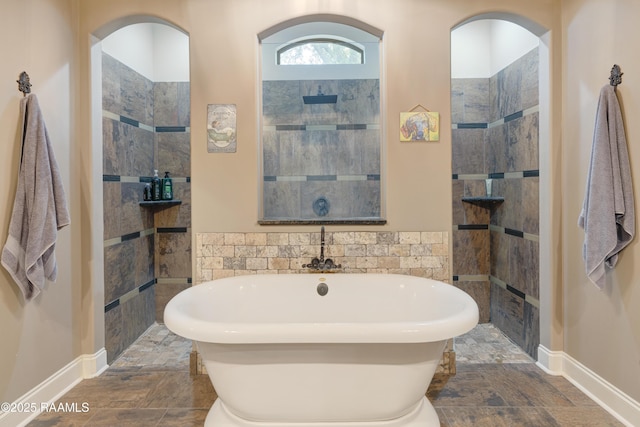 bathroom with tile walls, walk in shower, a freestanding tub, and stone finish flooring