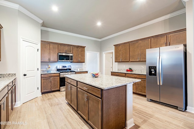 kitchen featuring crown molding, light stone counters, a center island, light wood-type flooring, and stainless steel appliances