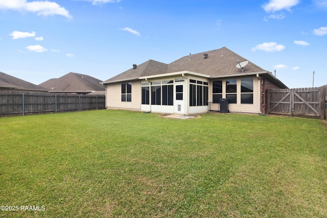 rear view of house featuring a sunroom, a yard, a fenced backyard, and a gate
