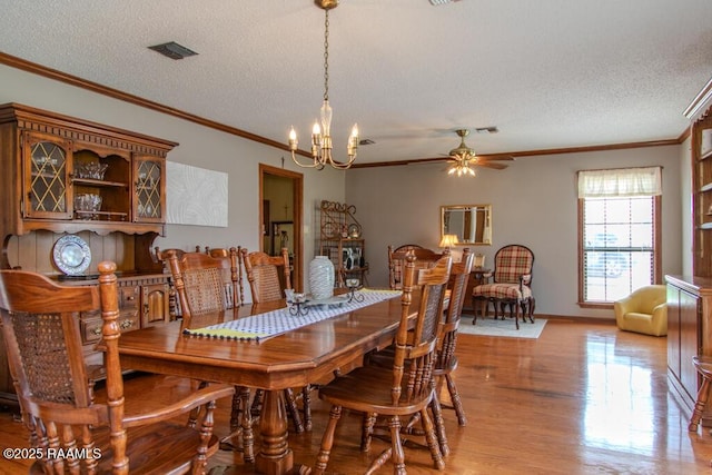 dining area with light wood-style flooring, ceiling fan with notable chandelier, crown molding, and a textured ceiling