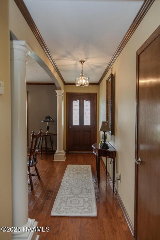 entrance foyer with a notable chandelier, dark wood-style floors, ornate columns, and crown molding