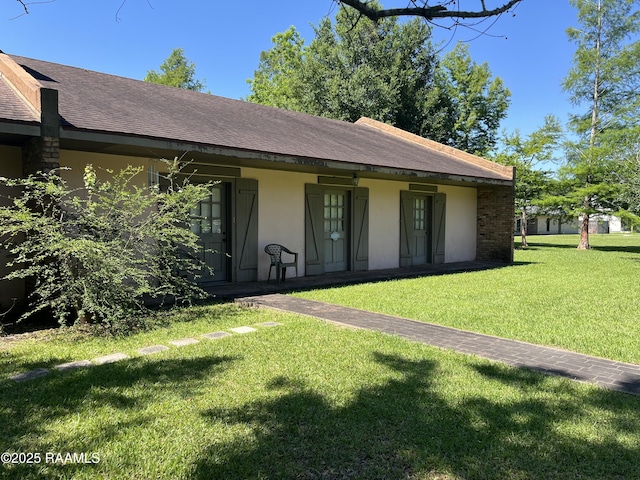view of front facade featuring roof with shingles, stucco siding, and a front yard
