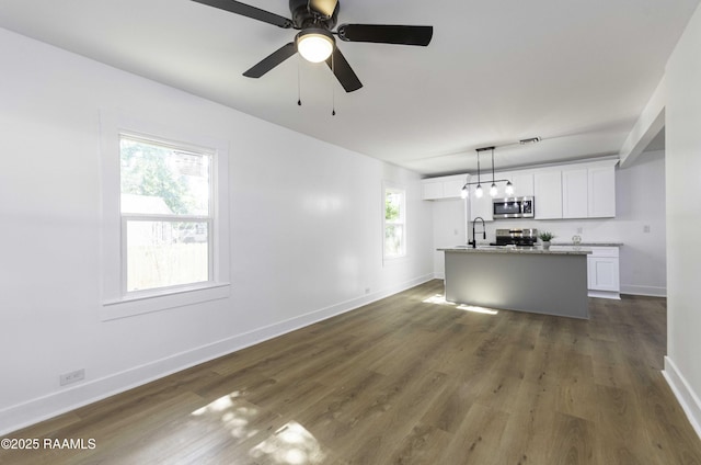 unfurnished living room featuring a ceiling fan, visible vents, a sink, baseboards, and dark wood-style floors