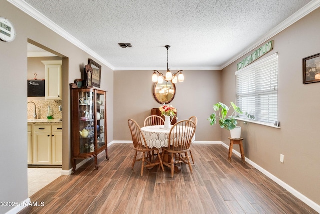 dining space featuring a textured ceiling, light wood-type flooring, baseboards, an inviting chandelier, and crown molding