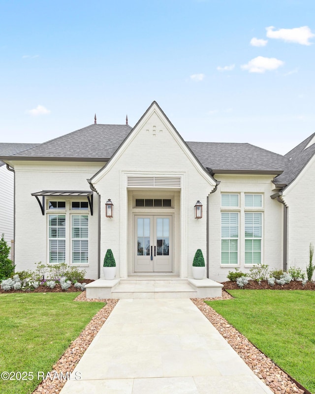 211 Crossbill Dr, Lafayette, LA 70508 - view of exterior entry featuring french doors, brick siding, roof with shingles, and a yard