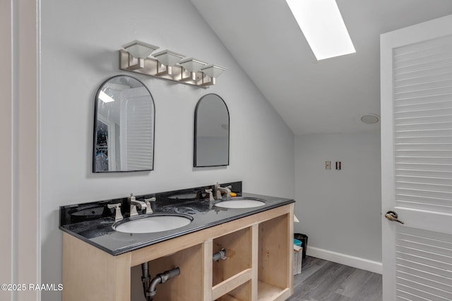 bathroom featuring vaulted ceiling with skylight, baseboards, a sink, and wood finished floors