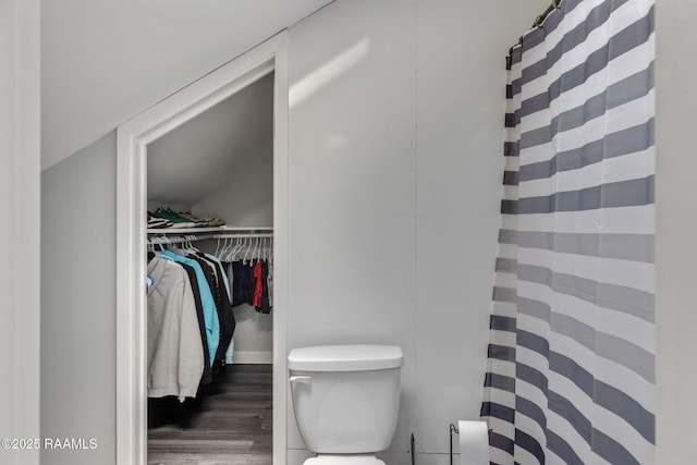 bathroom with a spacious closet, a shower with shower curtain, toilet, and wood finished floors